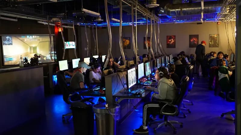 Wide venue view: busy LAN floor with big projector screen showing CS, blue LED ceiling and poster wall